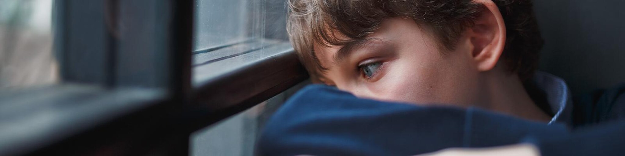 Junge schaut traurig aus dem Fenster